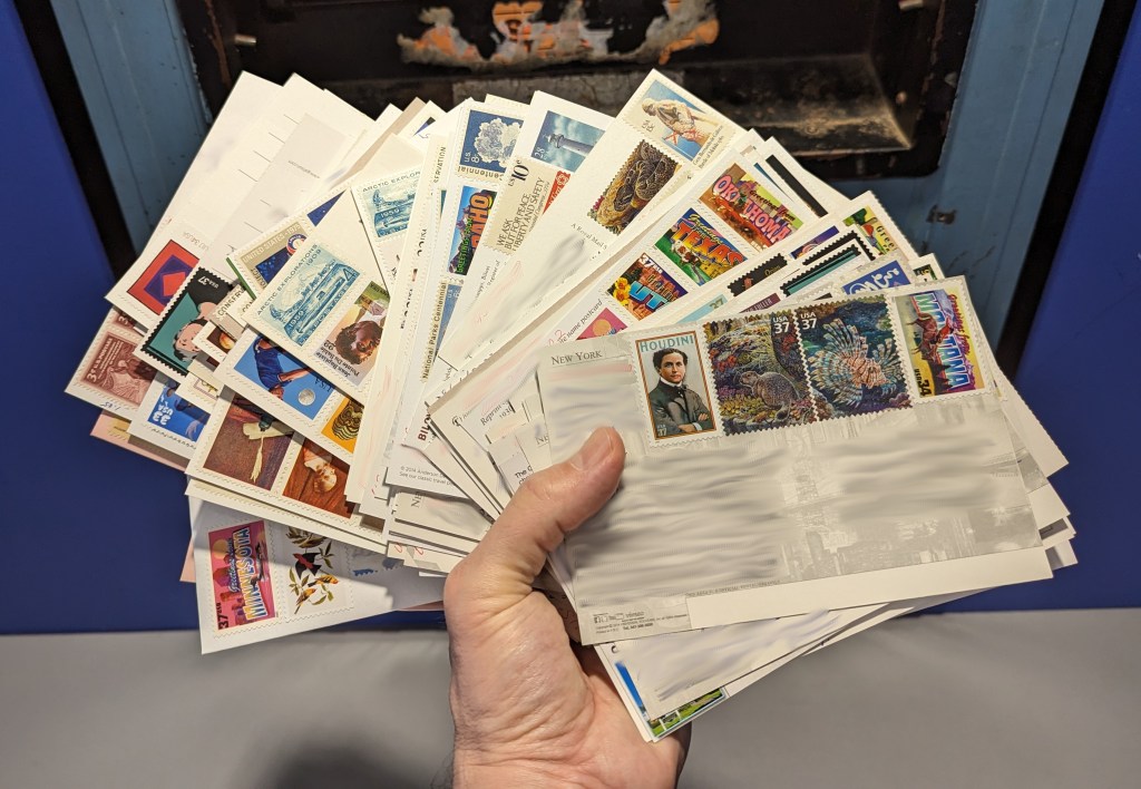 Hand holding 100 postcards in front of a mail drop.