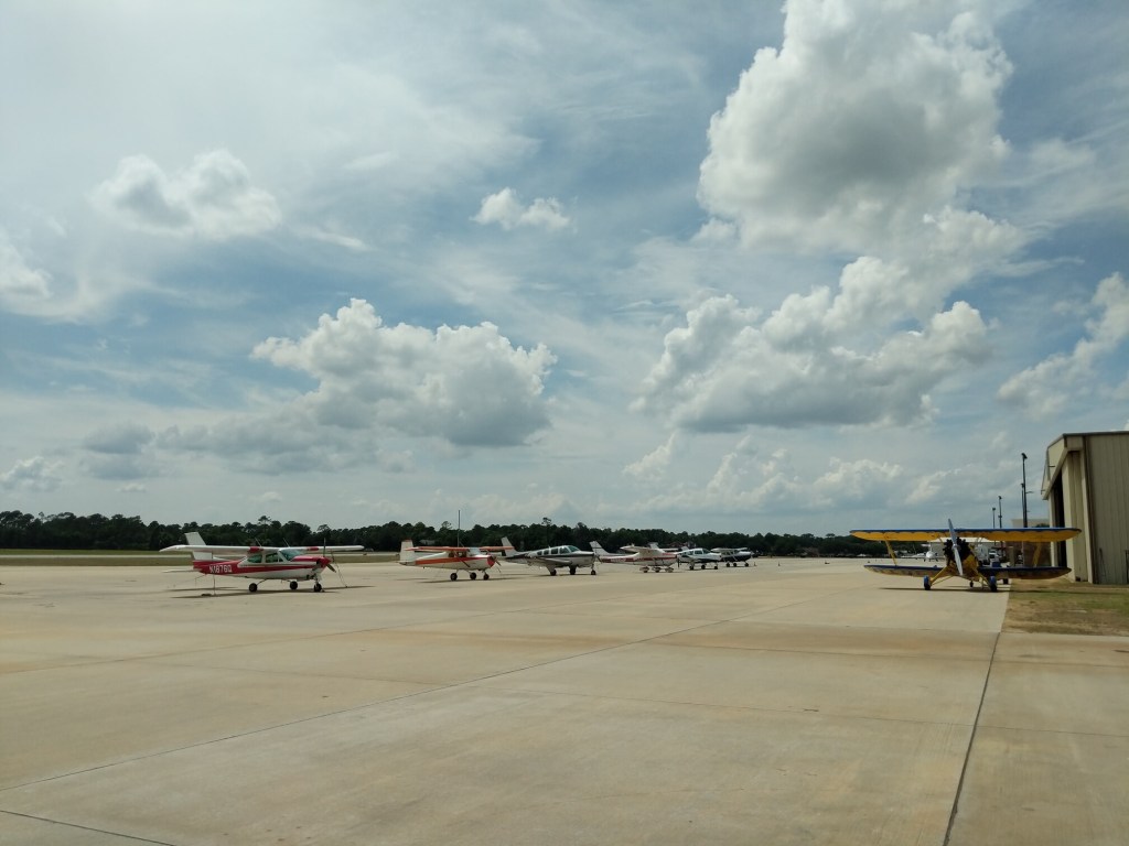 Parked line of Cessna and Beechcraft light aircraft on the left and Coastal Biplane Tour's Waco UPF-7 on the right at St. Simons Island Airport at McKinnon Field, May 2019.