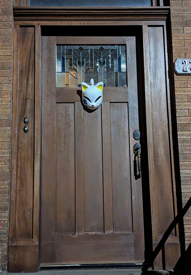 Kitsune-style cat mask hanging on a wooden exterior door of a house in Park Slope, Brooklyn, New York