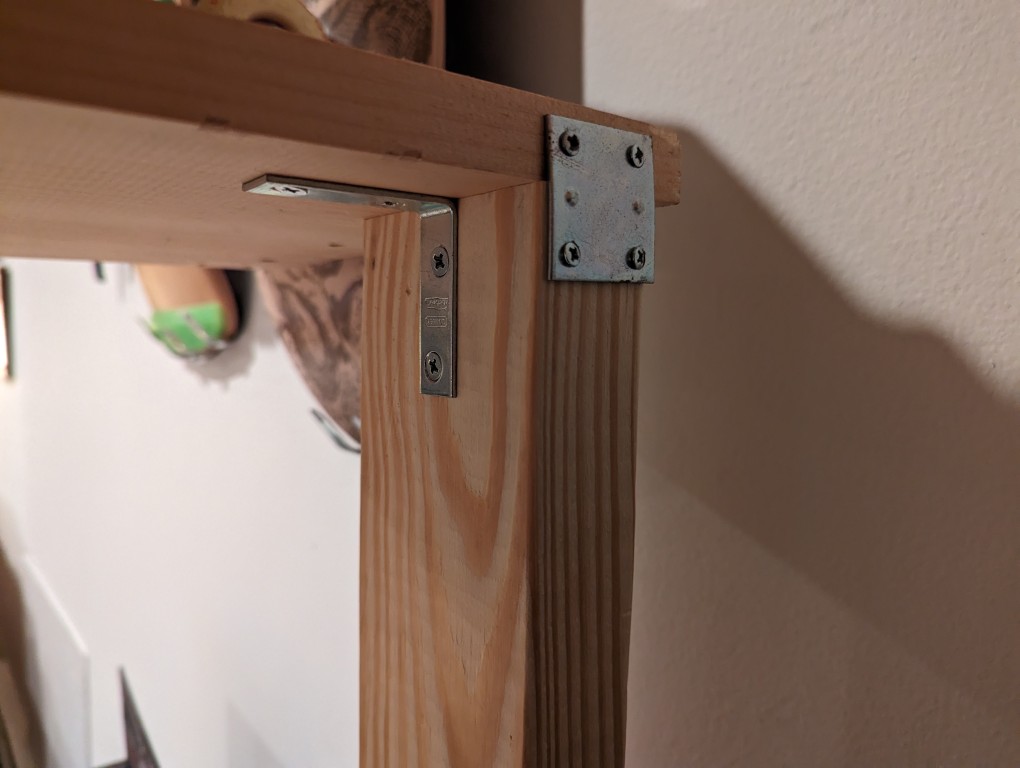 Metal plate and L-shaped bracket supporting the meeting of a 2" x 4" support and 1" x 12" x 48" board