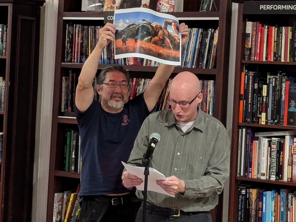 Jay Werkheiser and Frank Wu standing by a microphone and reading from a text.