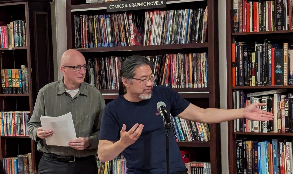 Jay Werkheiser and Frank Wu standing by a microphone and reading from a text.