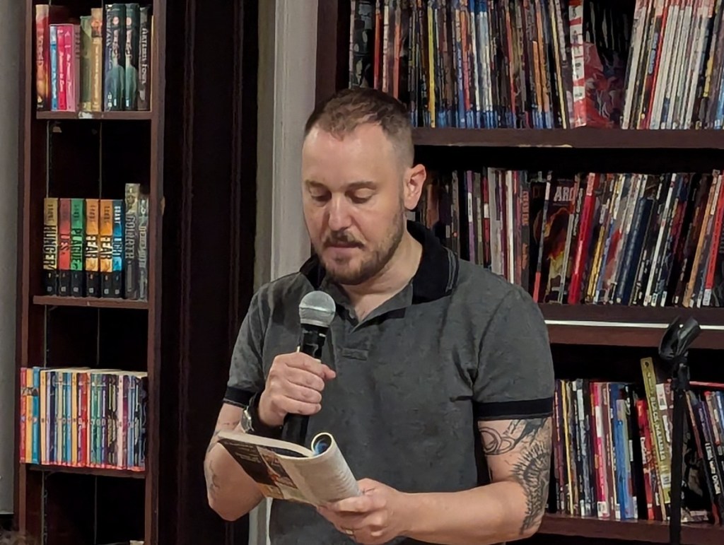 Sam J. Miller holding a microphone and reading from a text.