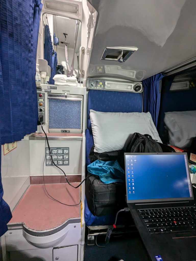 amtrak roomette seat filled with bags, laptop open on foldout table, toilet and sink on the left