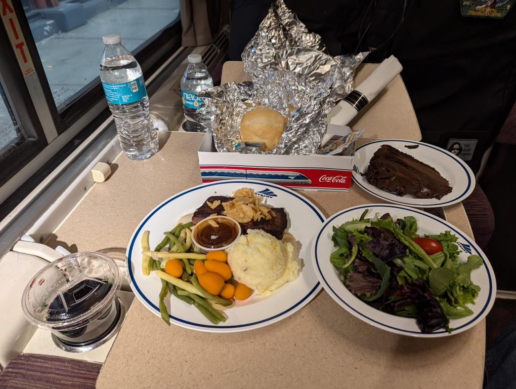 amtrak dinner service on foldout table in roomette--steak, potatoes, vegetables, salad, chocolate cake, roll, and red wine in plastic cup