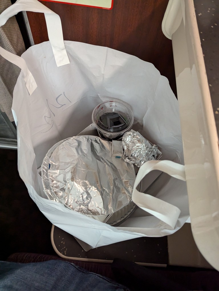 amtrak dinner service white plastic bag interior with plates wrapped with foil and plastic cup of red wine