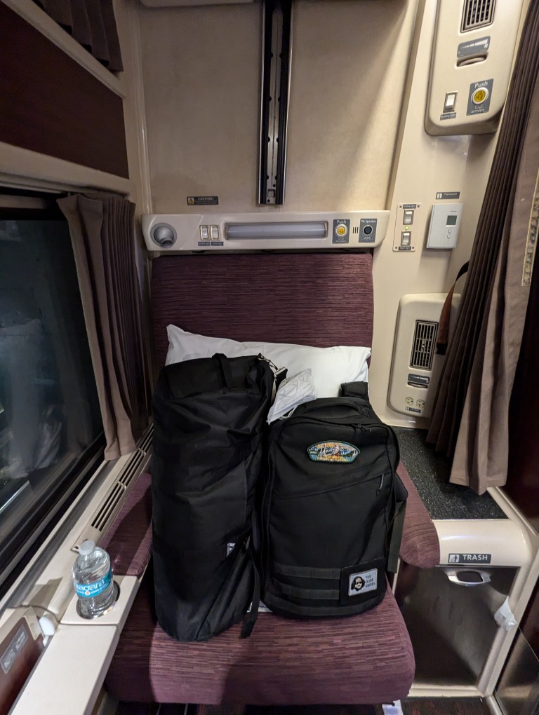 amtrak train roomette with seat occupied by two bags and a pillow