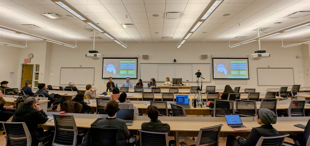 audience of people listening to a panel of five people read stories in a large auditorium-style classroom.
