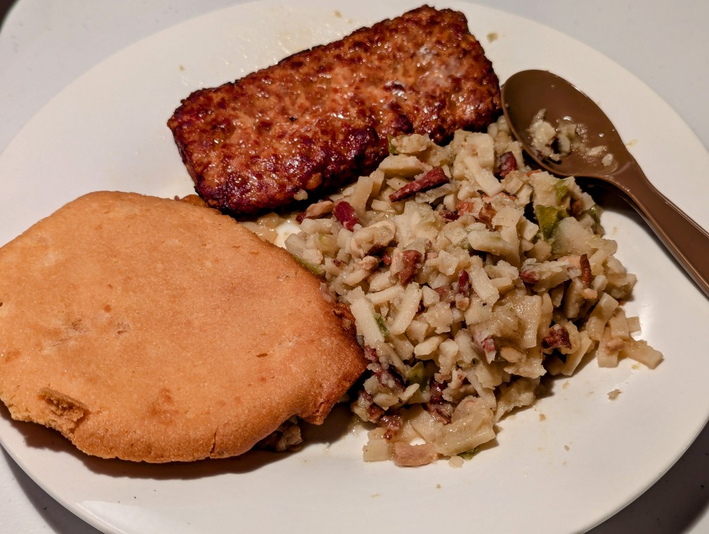 muffin top, pork patty, and hashbrowns on a white ceramic plate with plastic spoon