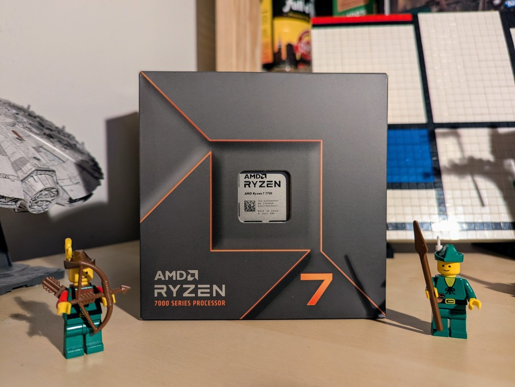 boxed amd ryzen 7 7700 cpu on a desk, lego forestmen on either side, millennium falcon and mondrian painting in lego in background