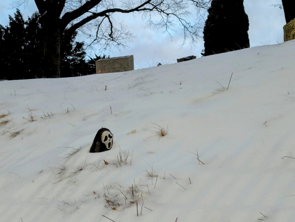 ghostface from the film scream is buried in snow with only his head poking through the snow drift