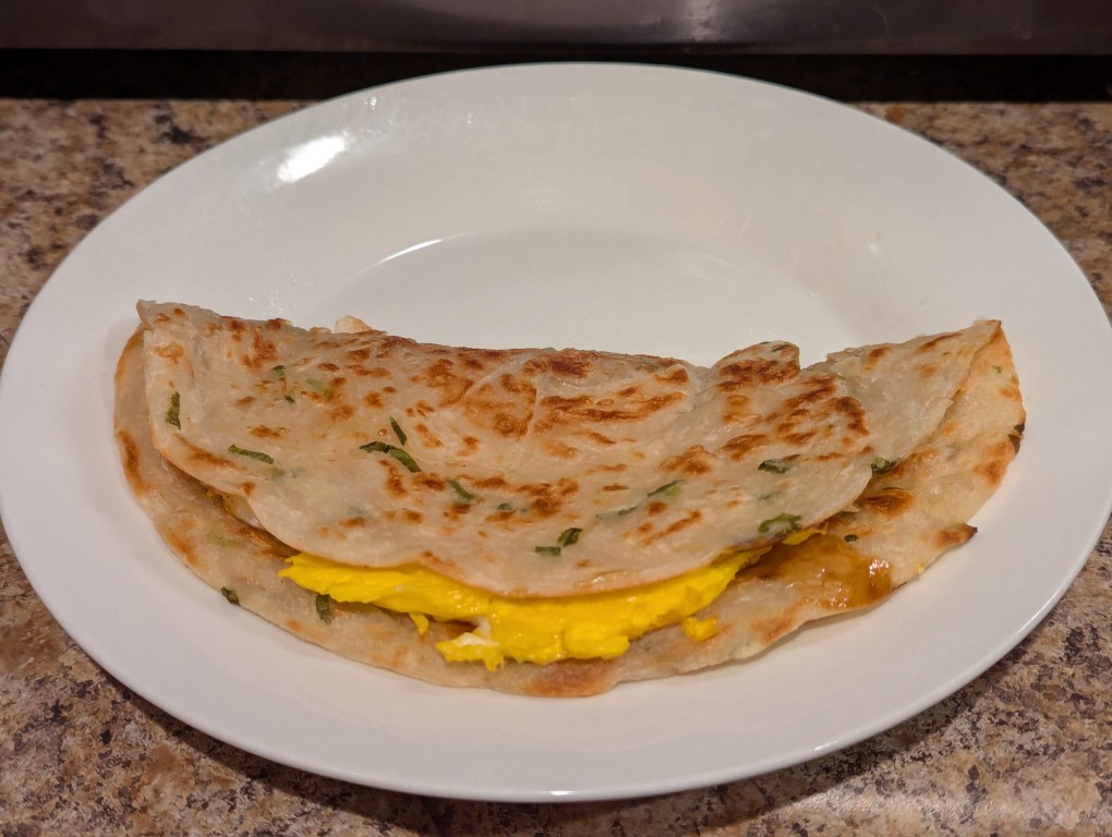 a green onion pancake with a fried egg and soy sauce paste folded inside resting on a white ceramic plate
