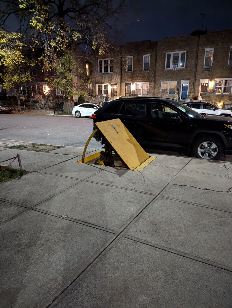 a metal cover is held open at about 45 degrees allowing access to a passageway built into the sidewalk going underground