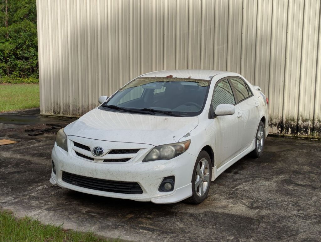 white 2013 toyota corolla with missing paint in spots, metal building in the background