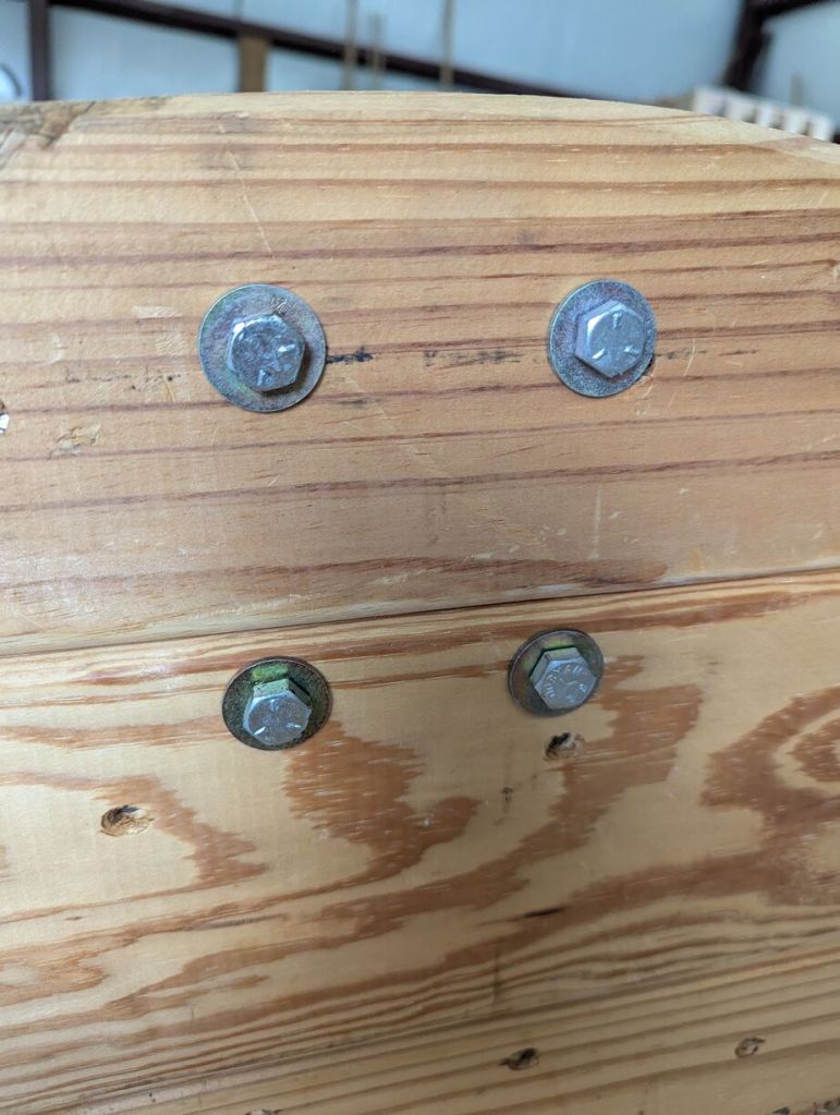 closeup of bolts and washers through lower surface of workbench holding the wheels on