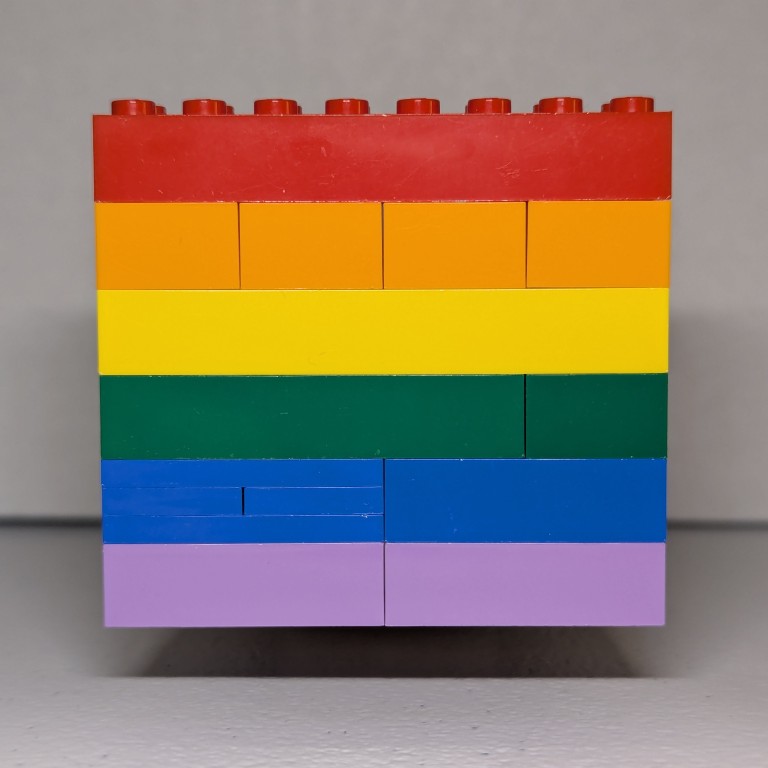 red, orange, yellow, green, blue, and purple pride flag made out of lego bricks in front of a white background