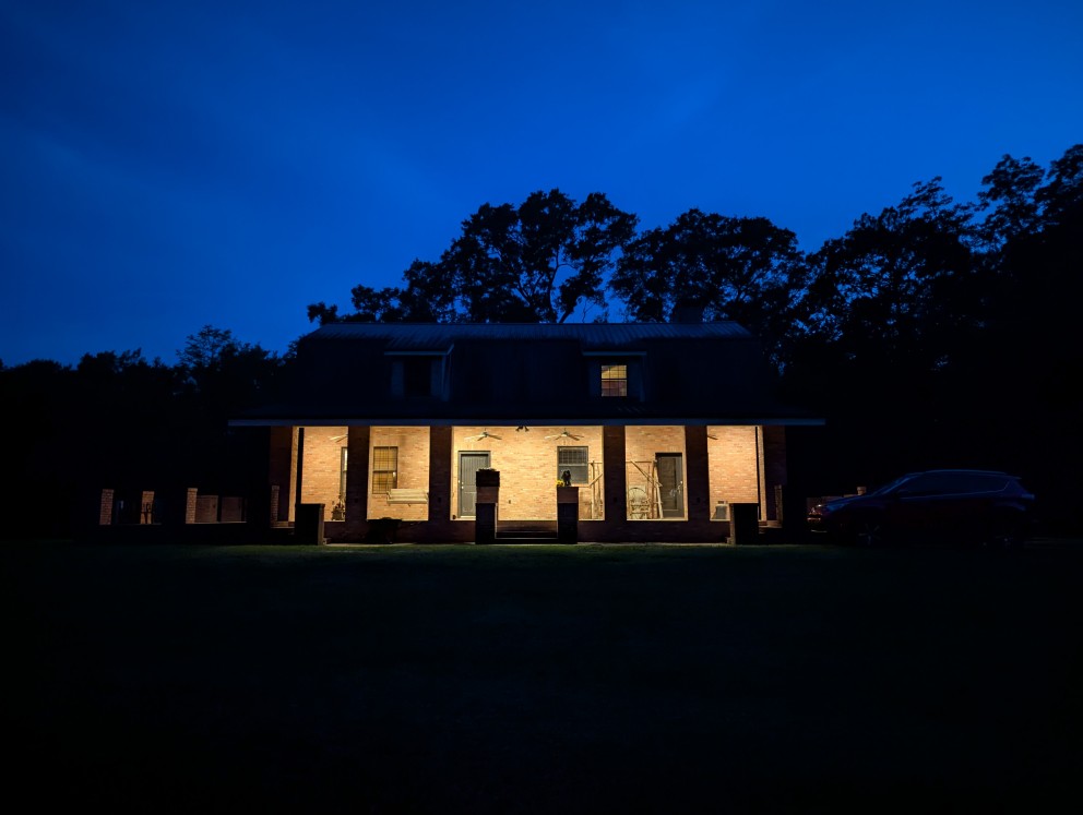 a barn roof house at night illuminated by porch light, trees in the background,