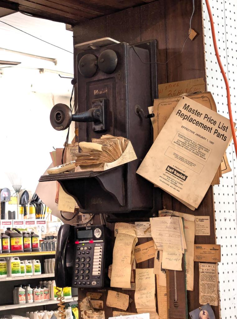 an antique telephone mounted on a wall above a modern corded phone