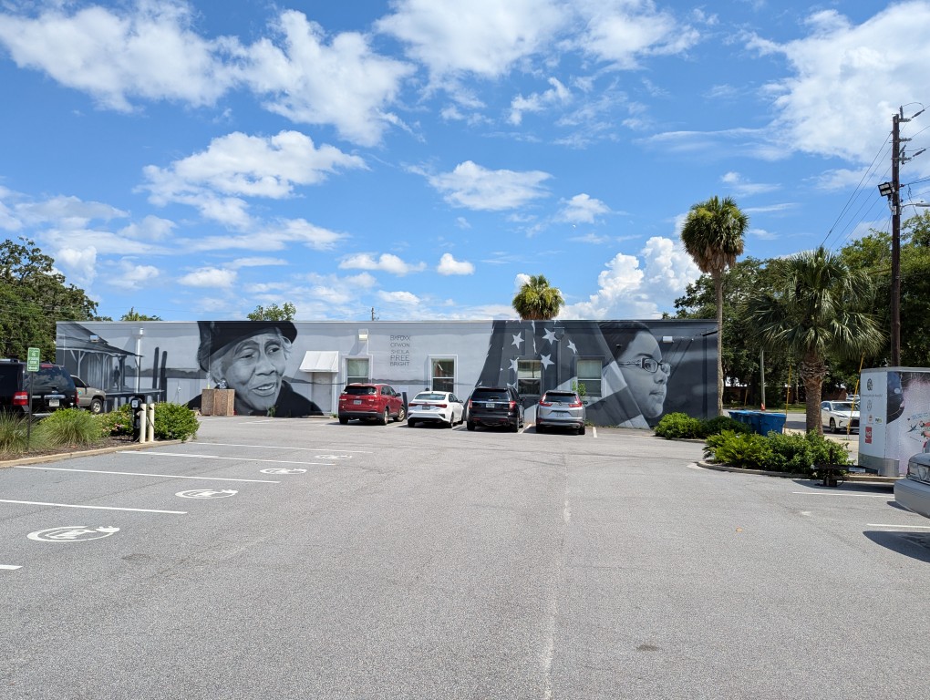 a building with a mural of an old woman, american flag, and child on the side of long building