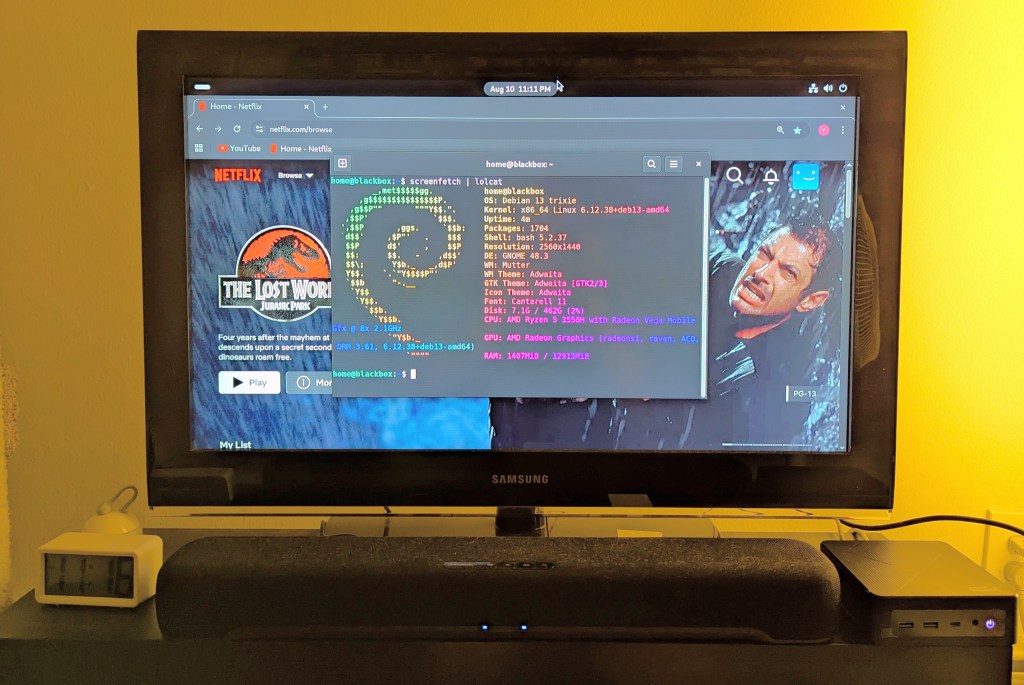 samsung tv and soundbar with a mini pc on the right side of the tv stand. the screen is showing netflix Jurassic Park the lost world in the background while the foreground terminal shows the pc's info, which is also in the second paragraph above.