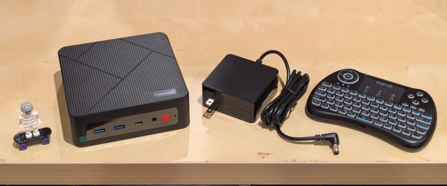 lego minifigure skeleton on skateboard next to origimagic c4 mini pc, power adapter, and handheld keyboard with trackpad