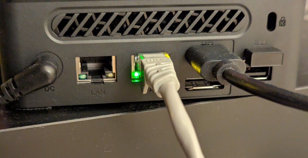 back of mini pc: power plug, two ethernet ports (one plugged in), HDMI (plugged in), display port, and 2 usb ports (one has a tiny device plugged in)