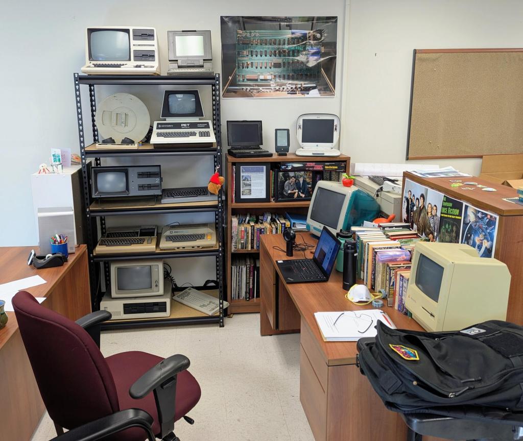 a small office space with shelves of computer and books and a desk covered with two computers and books