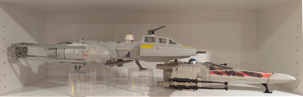 Star Wars vintage and modern action figures and vehicles on a bookshelf and desk.