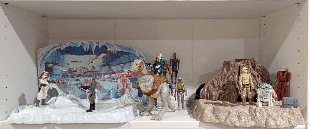 Star Wars vintage and modern action figures and vehicles on a bookshelf and desk.