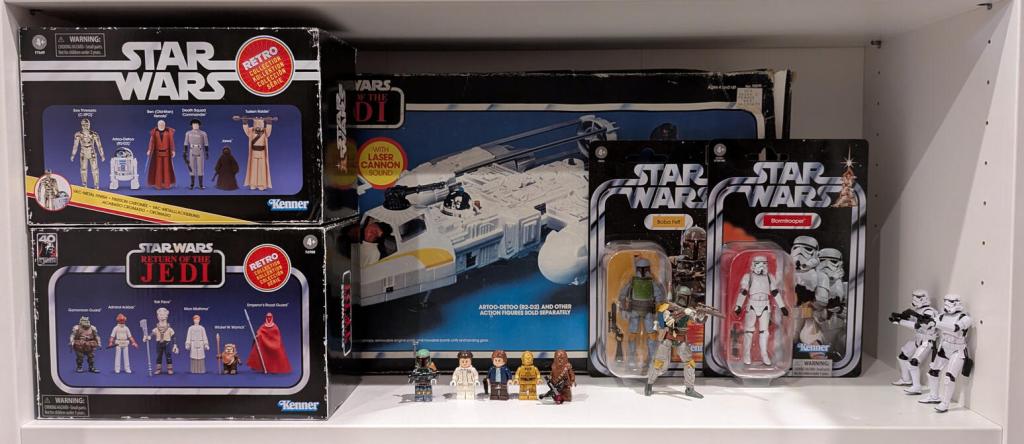 Star Wars vintage and modern action figures and vehicles on a bookshelf and desk.
