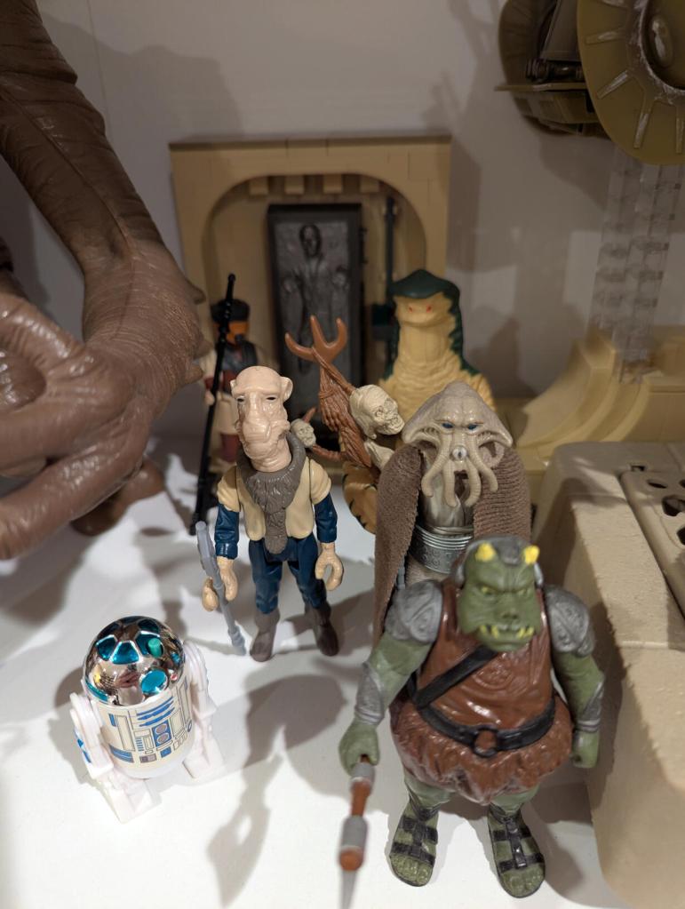 Star Wars vintage and modern action figures and vehicles on a bookshelf and desk.