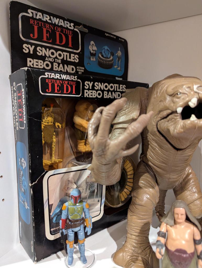 Star Wars vintage and modern action figures and vehicles on a bookshelf and desk.