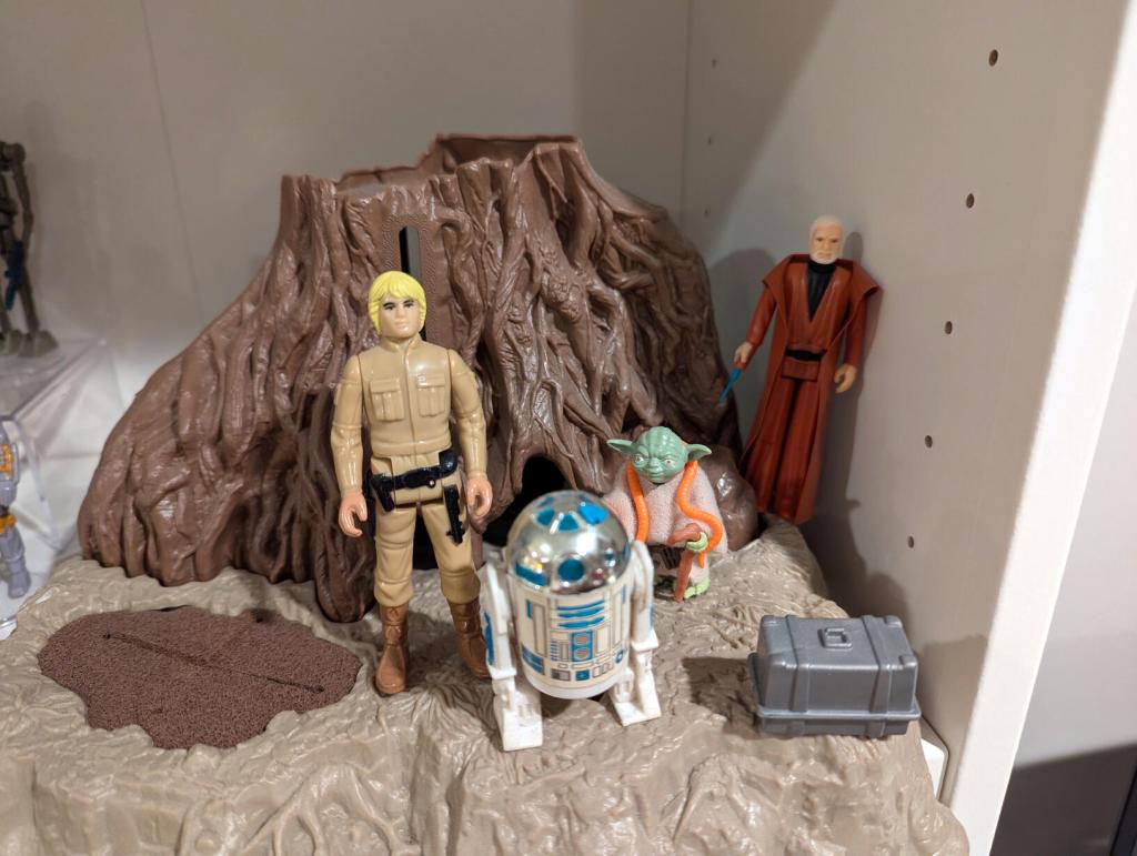 Star Wars vintage and modern action figures and vehicles on a bookshelf and desk.