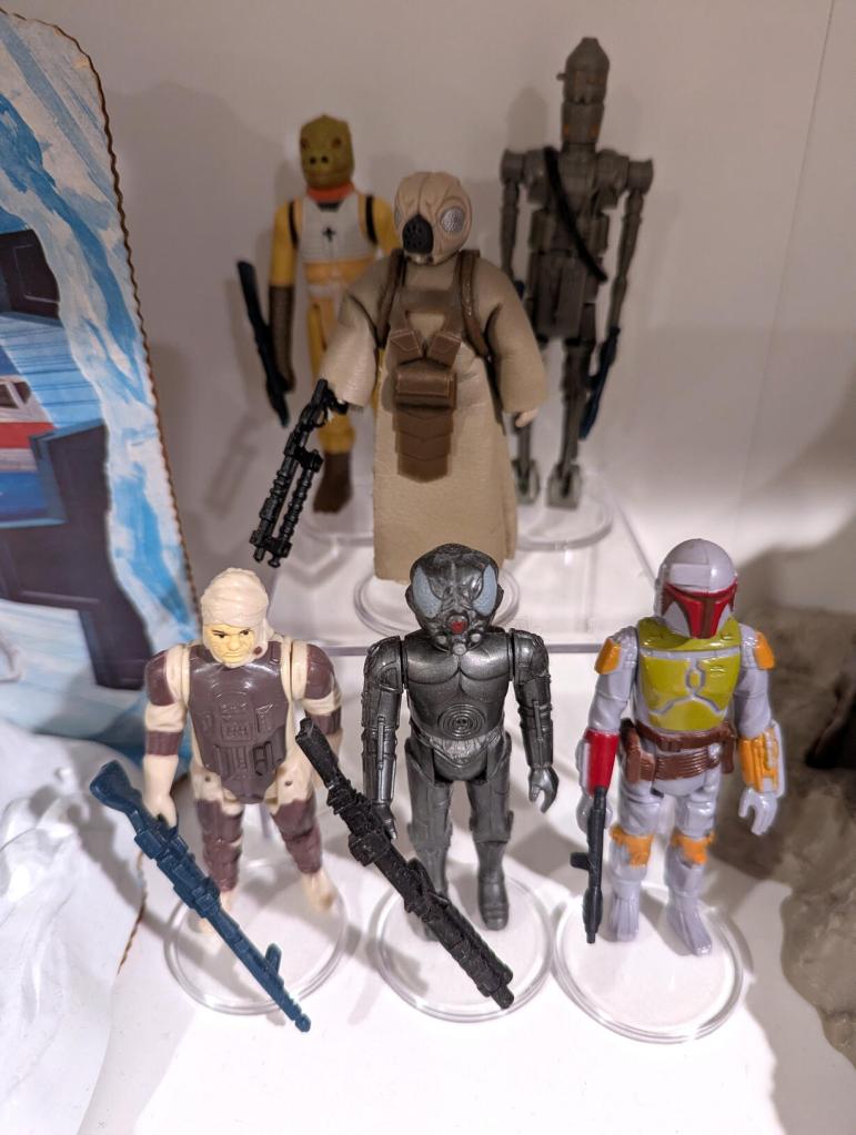 Star Wars vintage and modern action figures and vehicles on a bookshelf and desk.