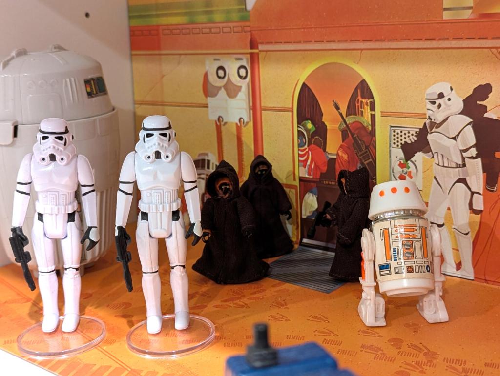 Star Wars vintage and modern action figures and vehicles on a bookshelf and desk.