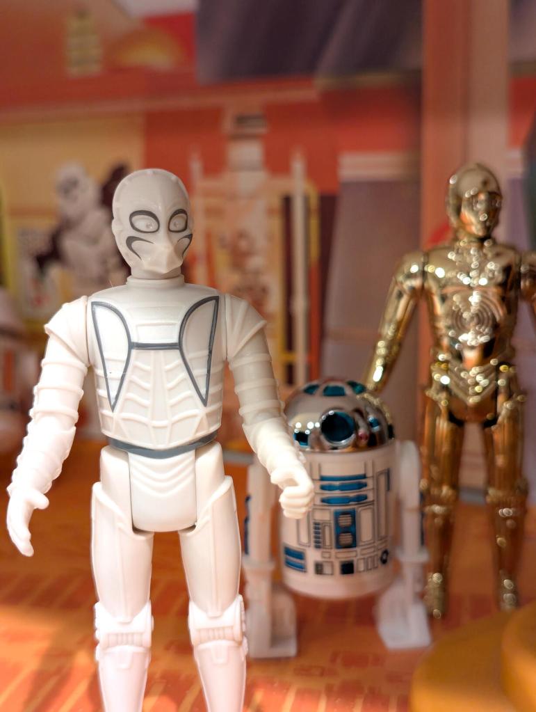 Star Wars vintage and modern action figures and vehicles on a bookshelf and desk.